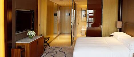 A hotel room with a large bed, a TV, a desk with a chair, and a bathroom visible through an open door.