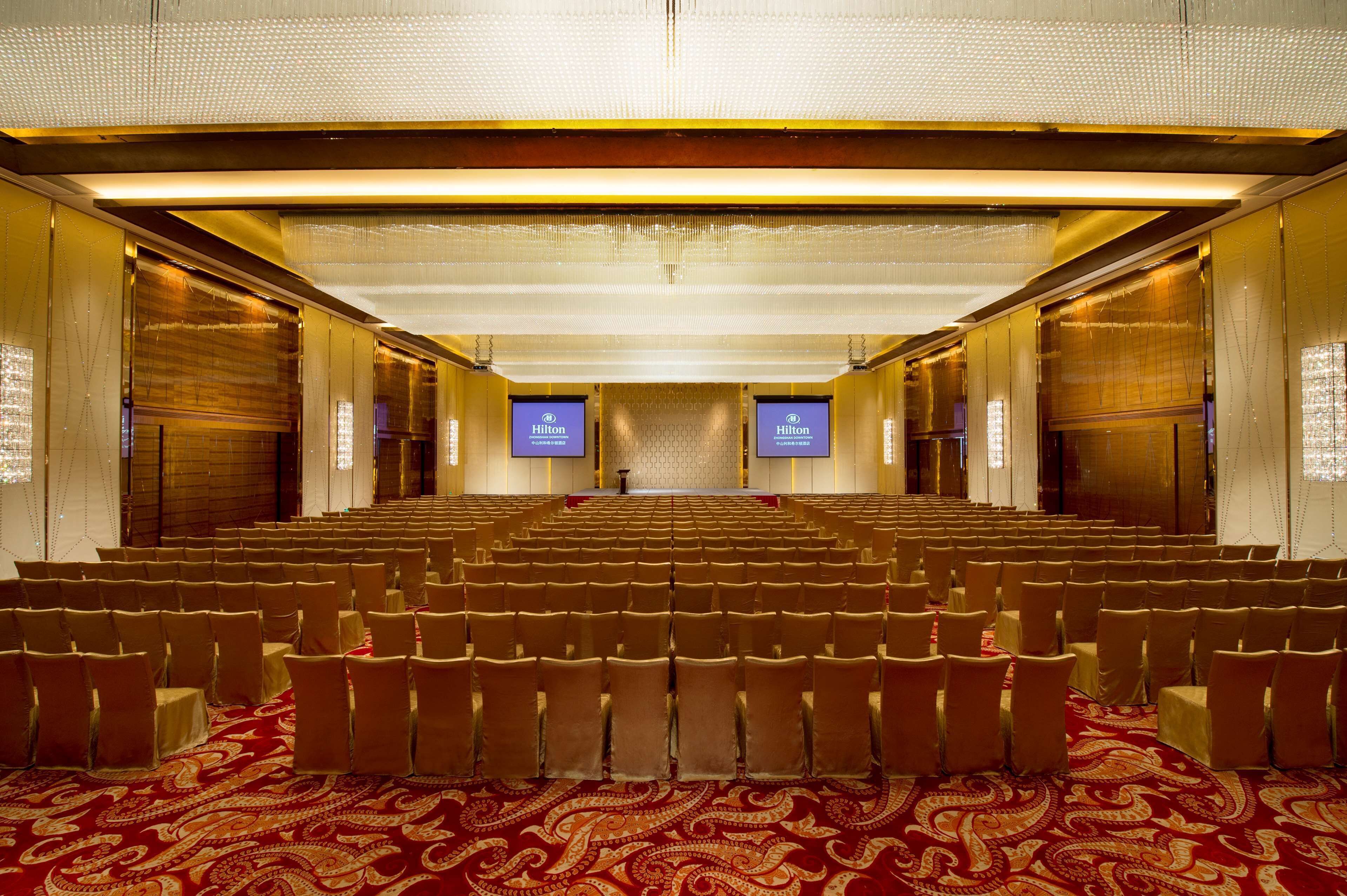 A large, well-lit conference room with rows of chairs and a red patterned carpet.