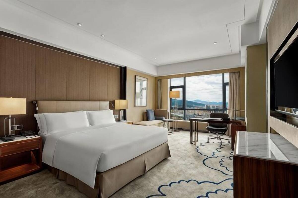 Habitación de hotel con una cama grande, un escritorio, una silla, un televisor y vistas a la ciudad.