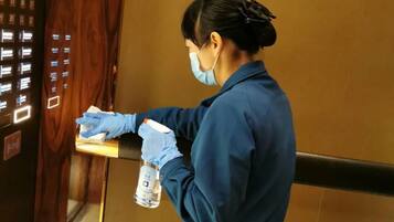 A person in a blue uniform cleaning an elevator with a spray bottle and cloth.