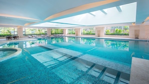 Una amplia piscina cubierta con agua cristalina, rodeada de tumbonas y una terraza con sol.