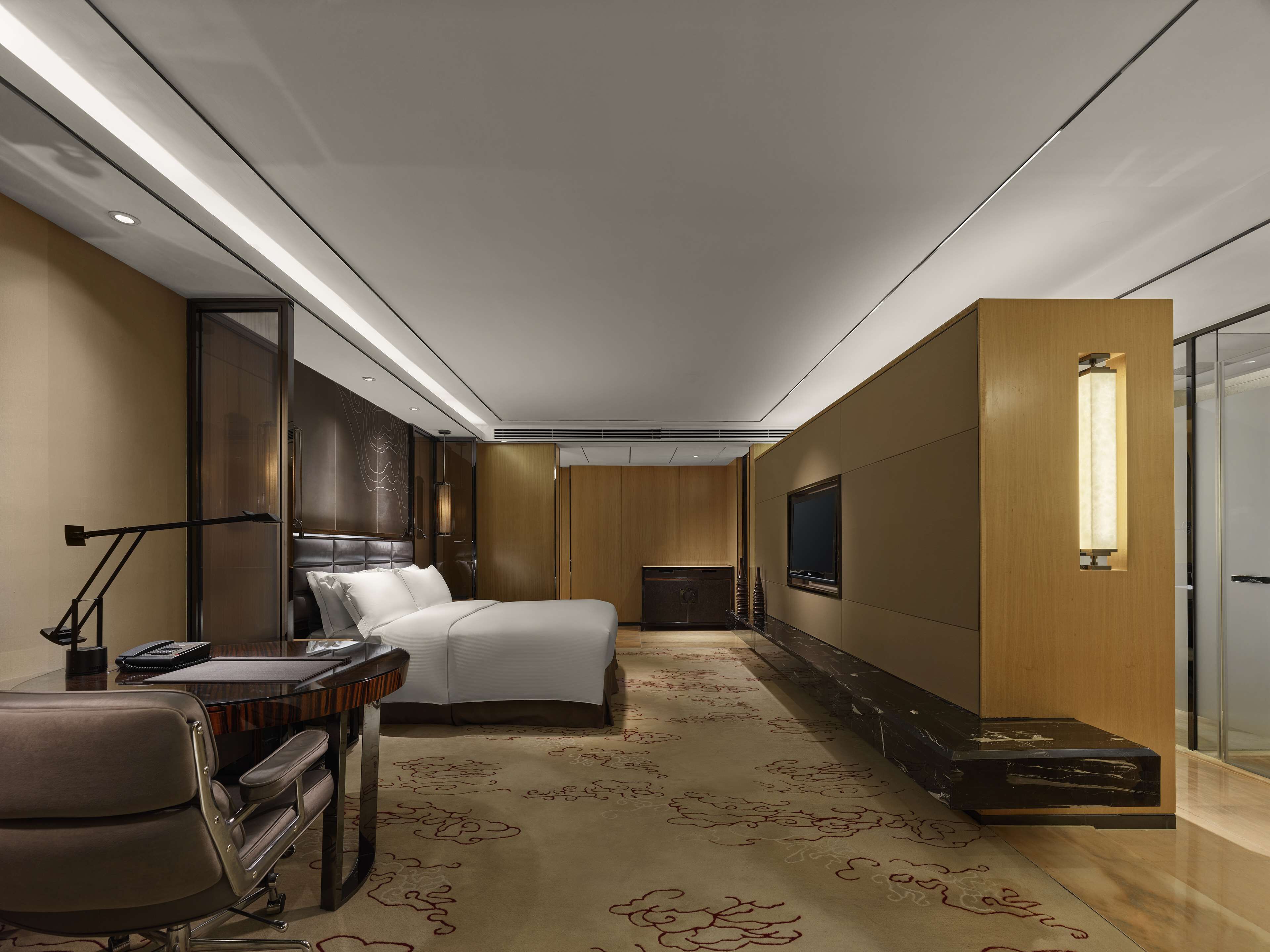 A modern hotel room with a bed, desk, chair, and a television.