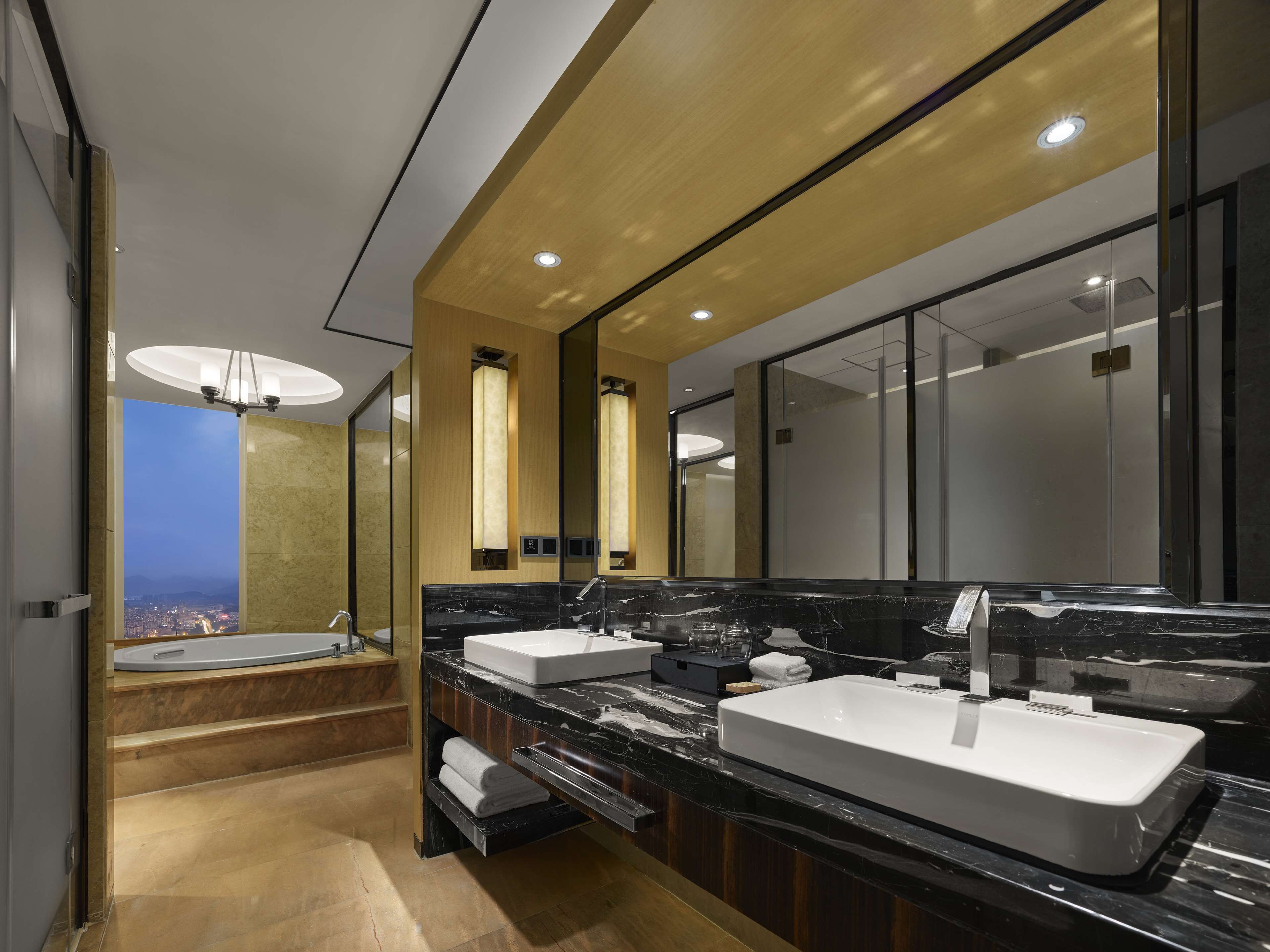 Un baño moderno con lavamanos dobles, un espejo grande y vistas de la ciudad a través de un ventanal.