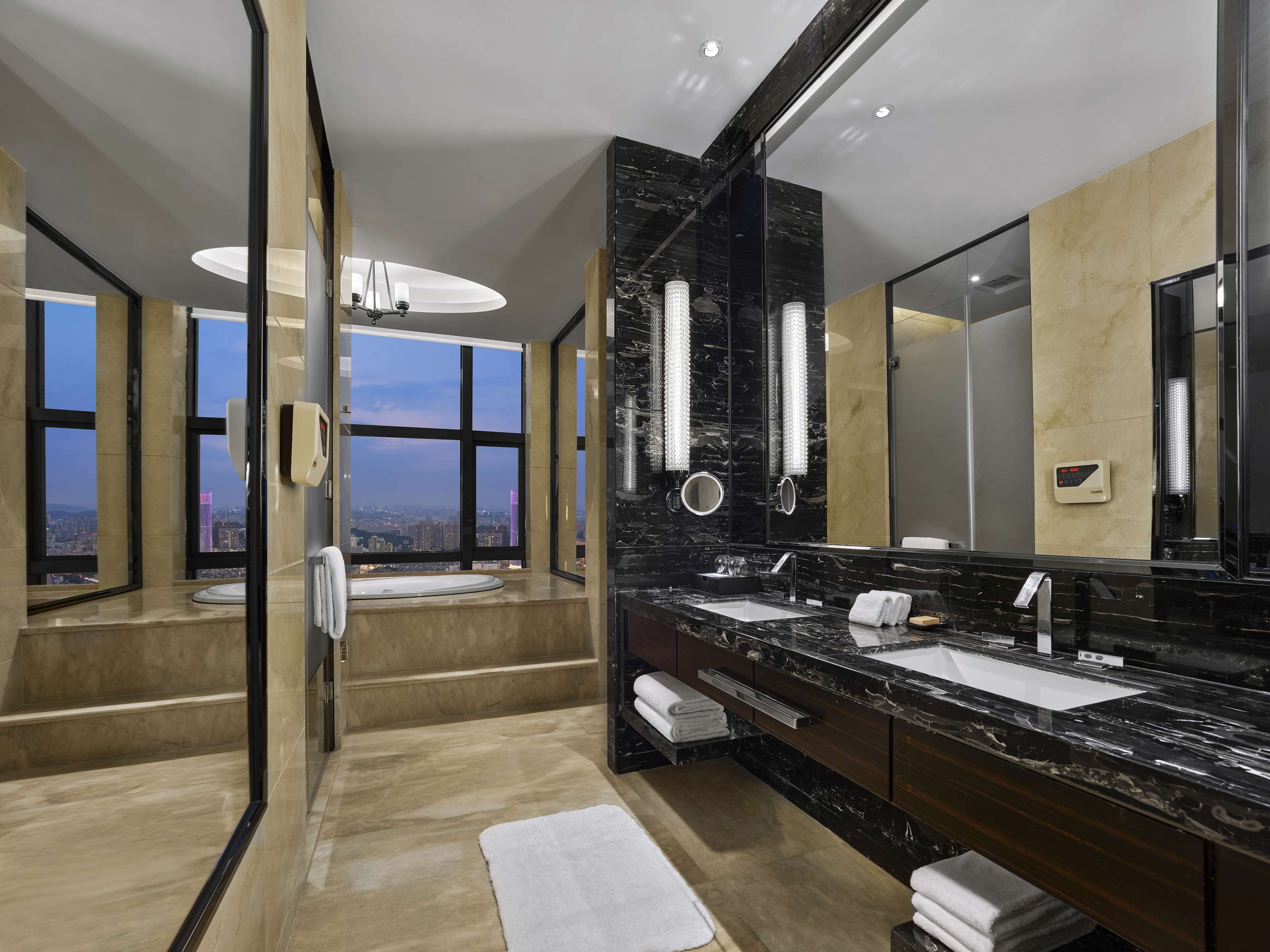 Un baño moderno con un espejo grande, lavamanos dobles y vistas a la ciudad a través de amplias ventanas.