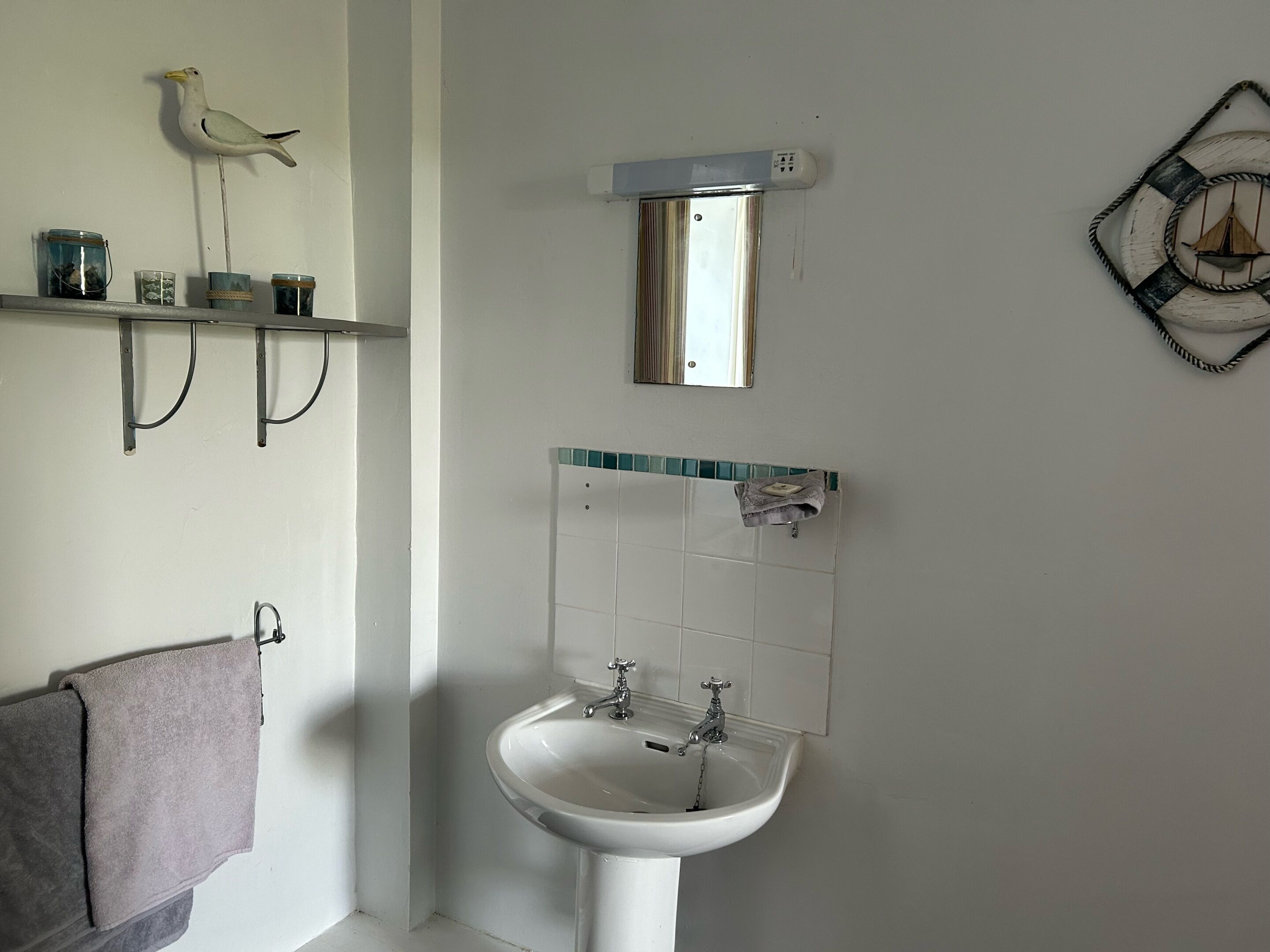 A bathroom with a white sink, a mirror, a towel rack, and a shelf with jars.