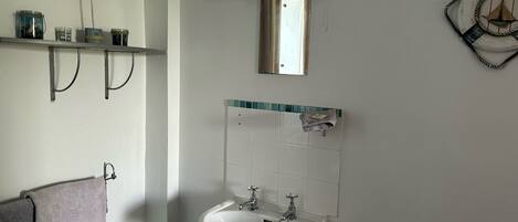 A bathroom with a white sink, a mirror, a towel rack, and a shelf with jars.