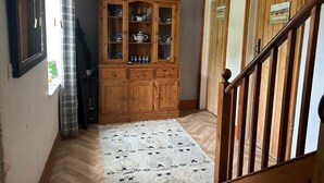 Un mueble de madera con puertas de cristal que exhibe vajilla y una tetera, una alfombra estampada en el suelo, y una escalera con barandillas de madera.
