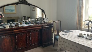 Una habitación con un aparador de madera, una mesa redonda con mantel floral y un espejo grande sobre el aparador.