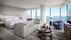 A hotel room with a bed, sofa, armchair, and a dining table with a bottle of champagne. - Ocean Casino Resort (Atlantic City)