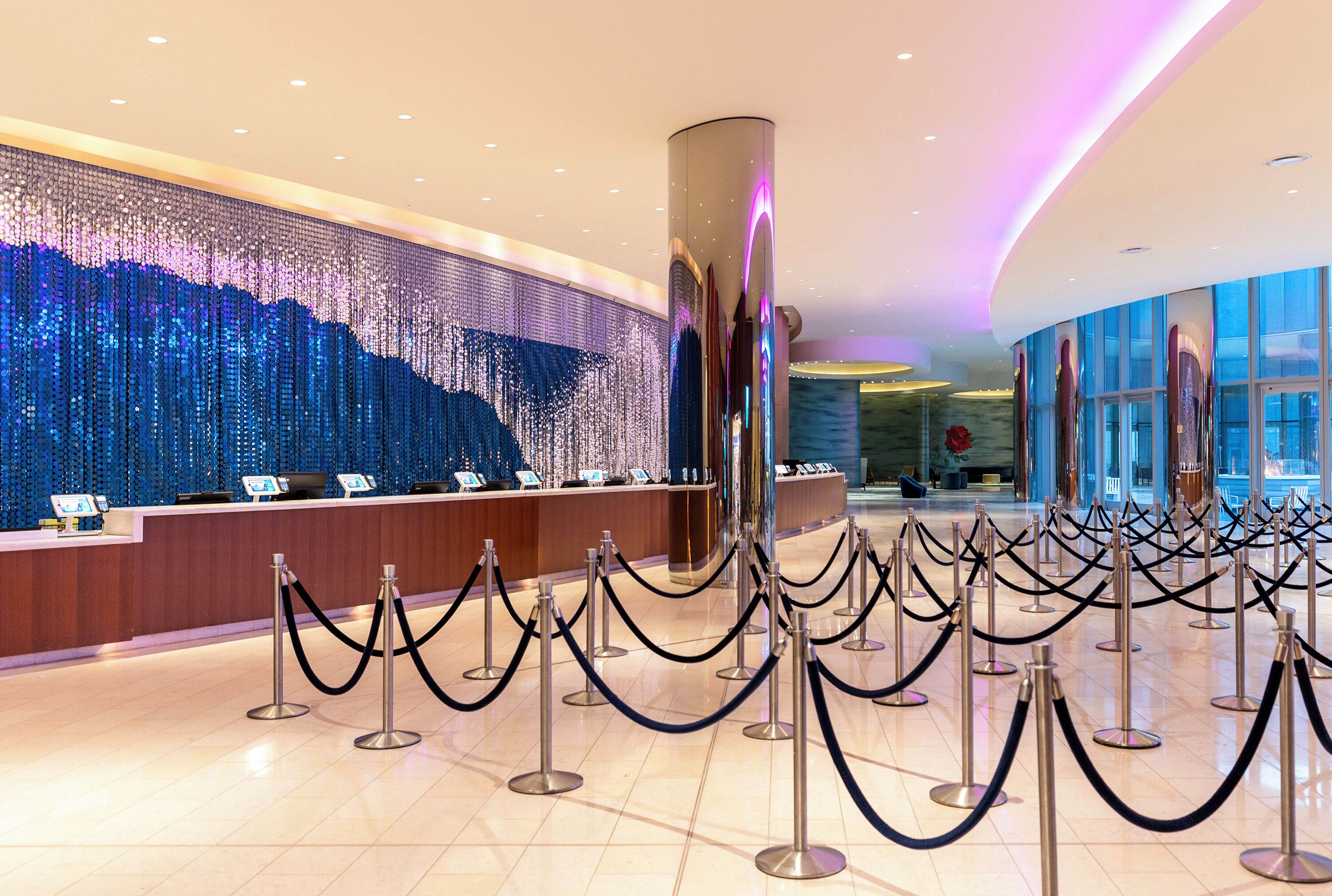 A hotel reception area with a decorative wall, a reception desk, and a queue of guests.