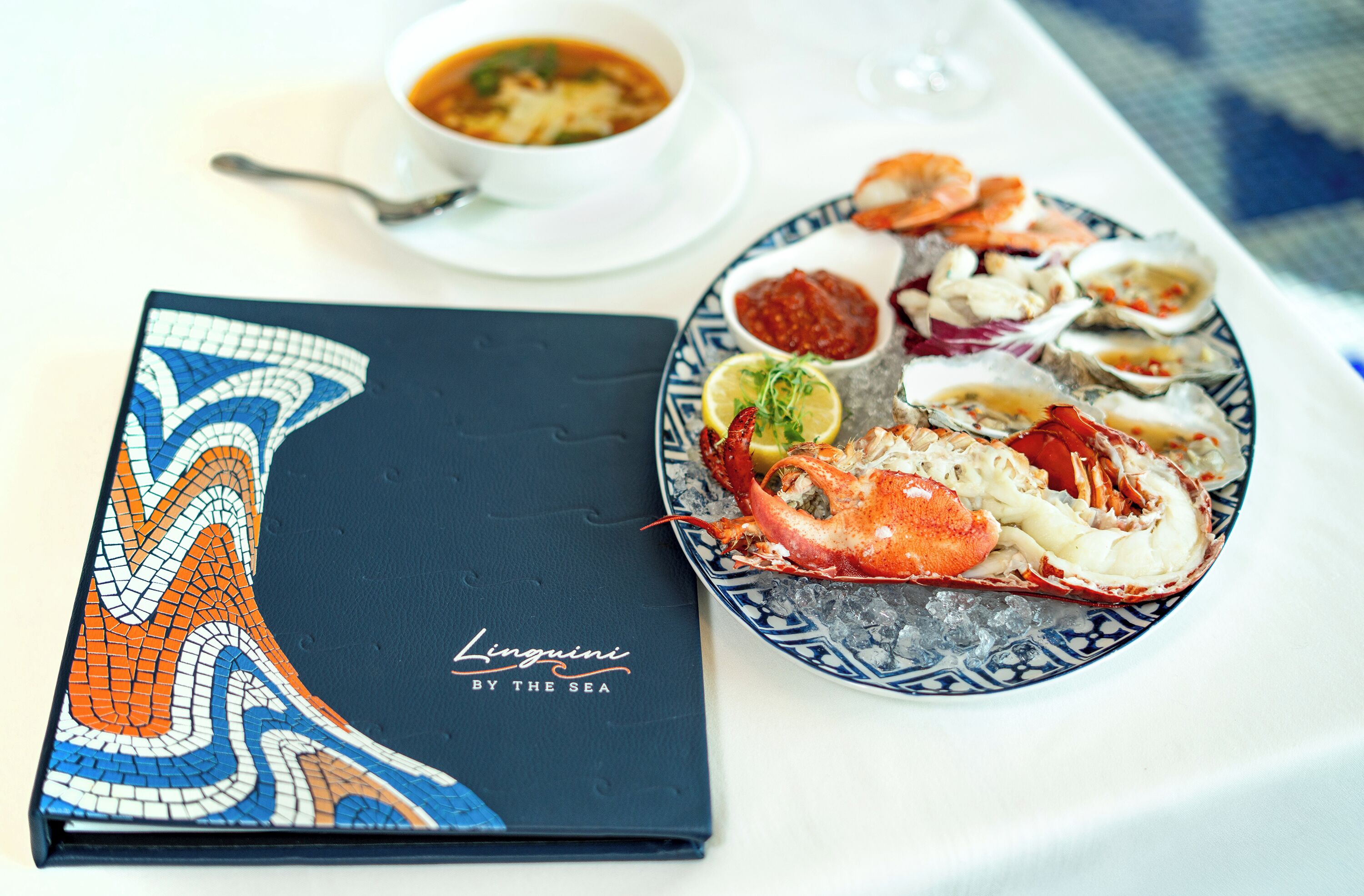 A seafood platter with various shellfish and a bowl of soup on a table.