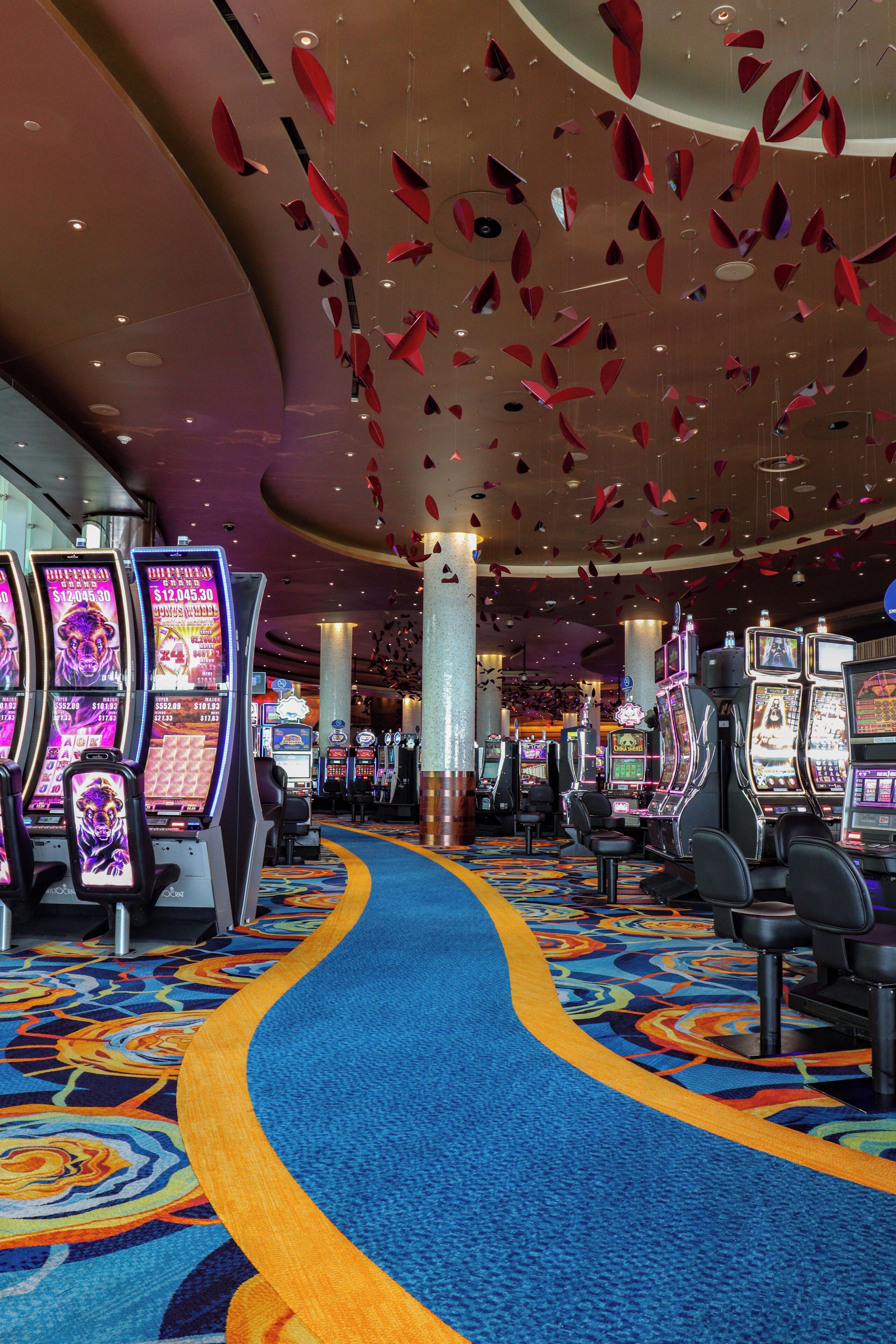 A casino interior with slot machines, a blue carpeted walkway, and red hanging decorations.
