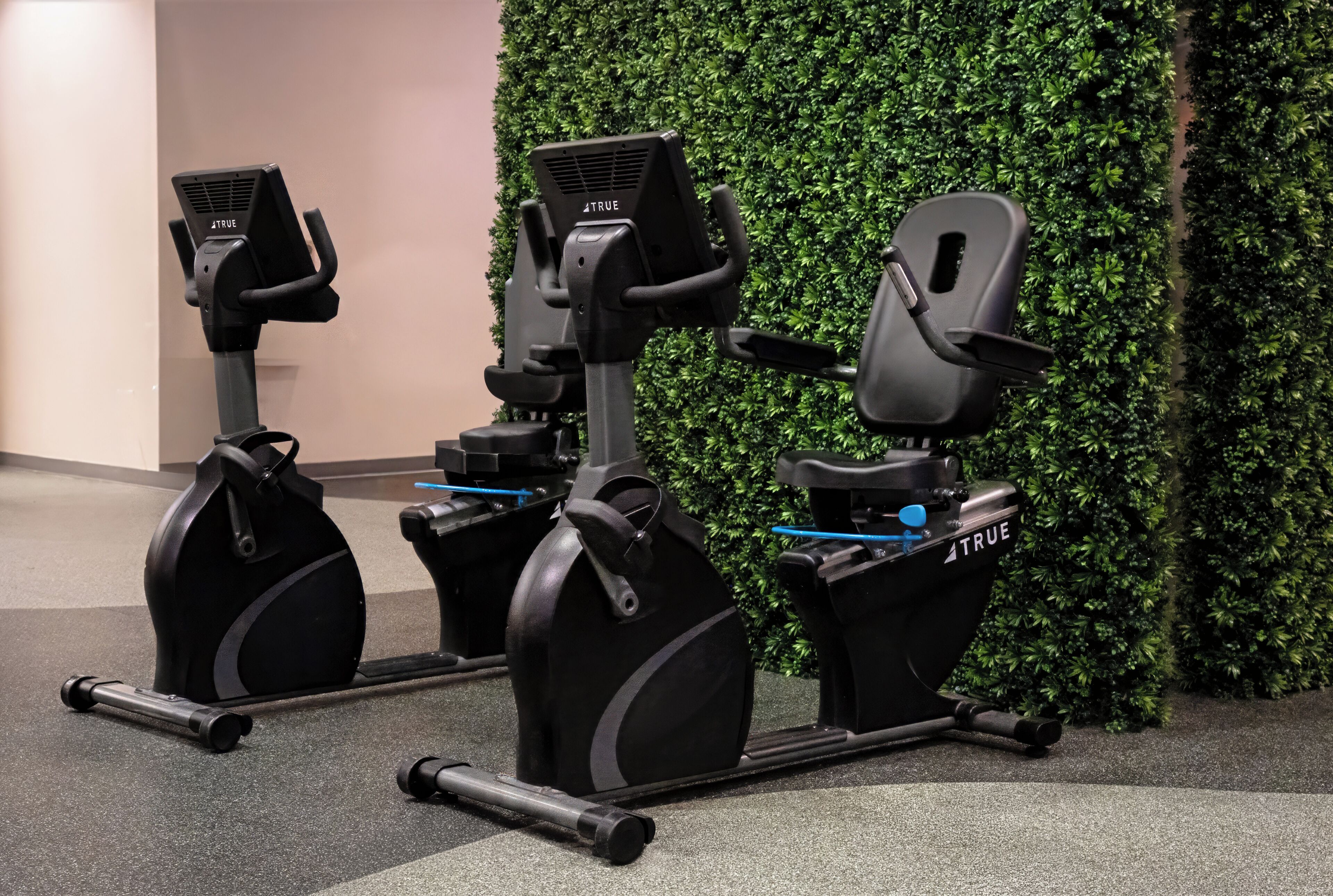 Two exercise bikes with 'TRUE' branding, positioned in front of a green wall.