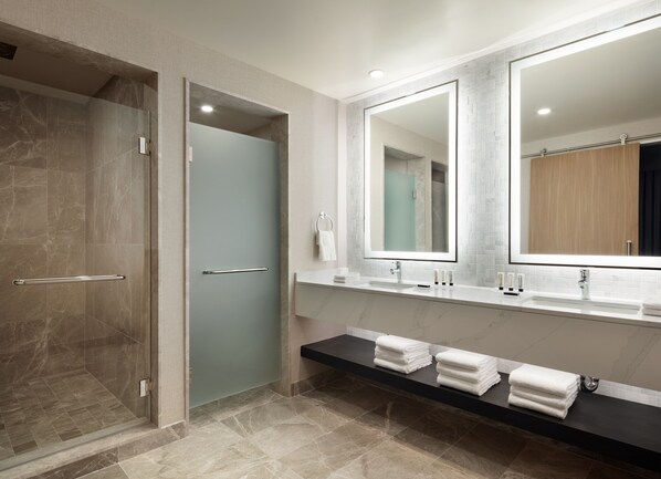 Un baño moderno con cabina de ducha de vidrio, tocador con un espejo grande y toallas dobladas con cuidado en un estante.