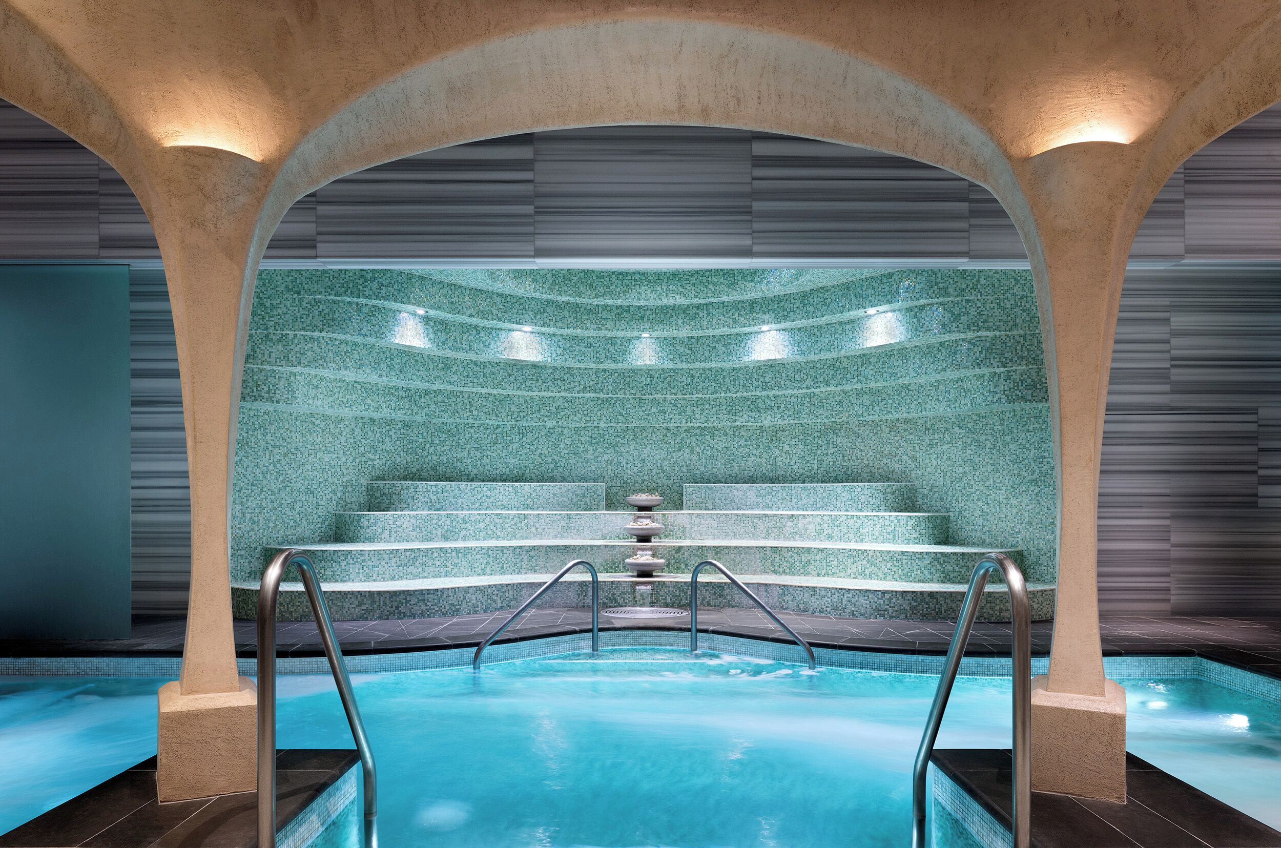 An indoor swimming pool with a stone wall and metal railings.