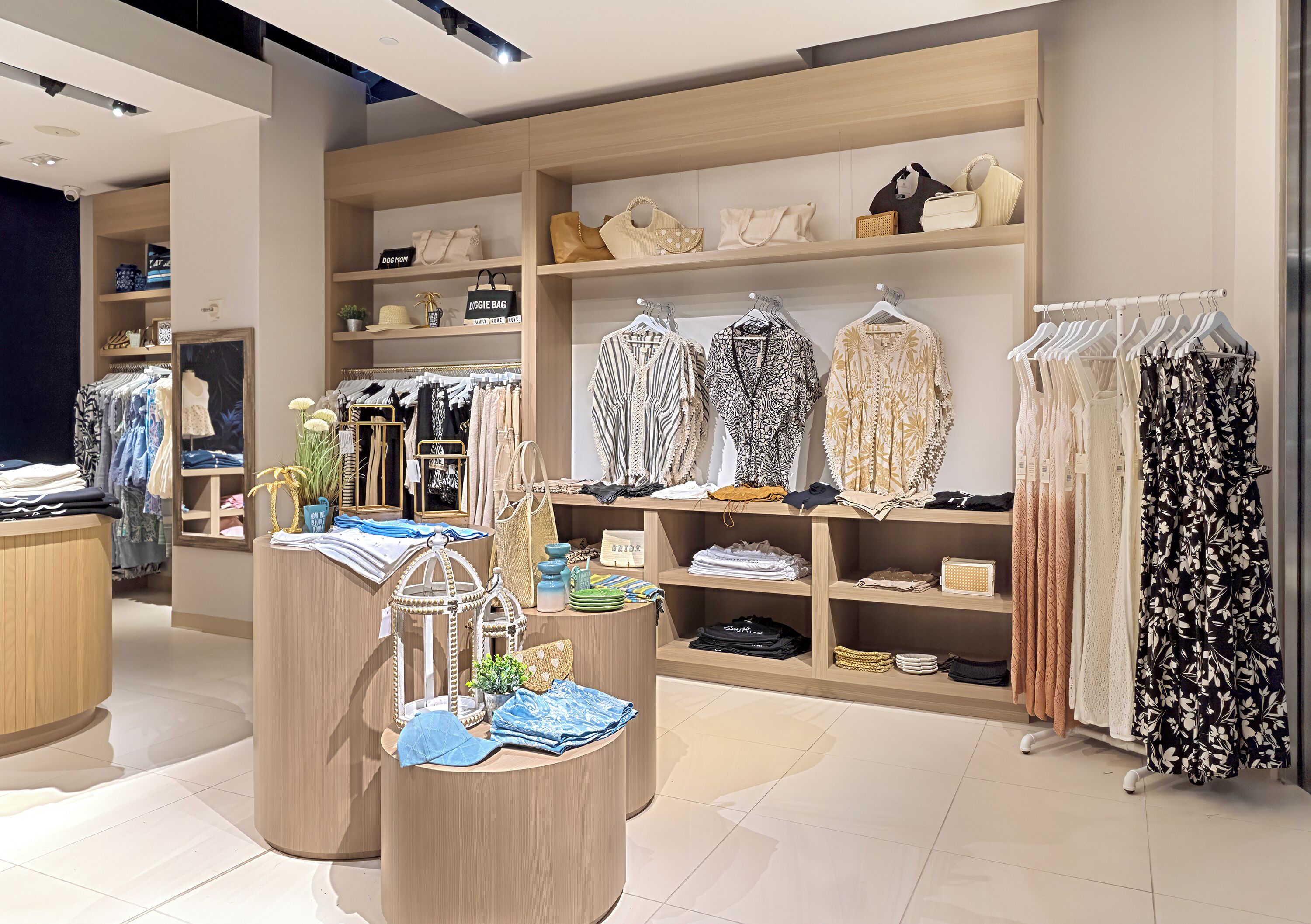 Un magasin de vêtements avec des étagères en bois, des portants remplis de vêtements et des sacs à main.