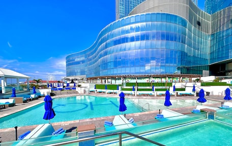A modern hotel with a large outdoor pool, lounge areas, and a distinctive curved glass building.
