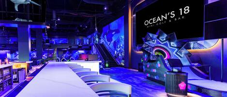 A bar with a long counter, chairs, and a large screen displaying 'OCEAN'S 18'.