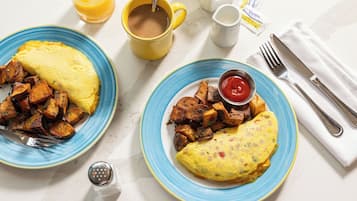 Two plates of food with a cup of coffee, a glass of orange juice, and condiments on a white table.