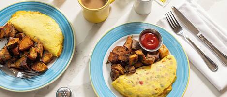 Two plates of food with a cup of coffee, a glass of orange juice, and condiments on a white table.