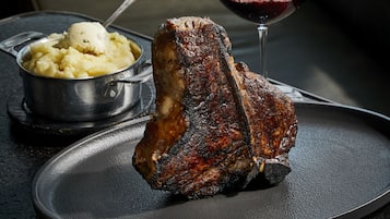 A steak with a side of mashed potatoes and asparagus on a plate, with a glass of red wine being poured.
