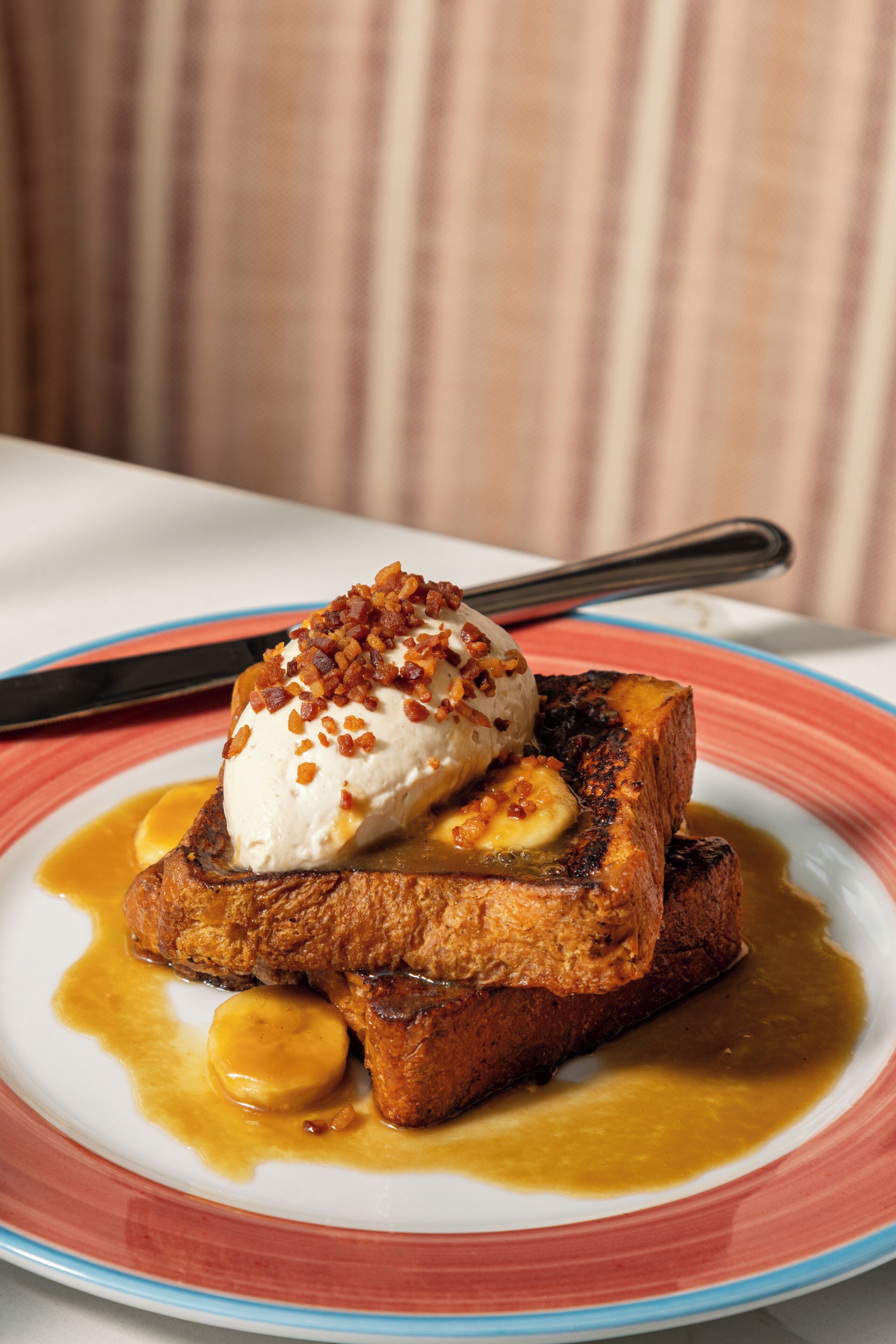 Un plato con tostadas francesas, una cucharada de crema batida y salsa de caramelo.