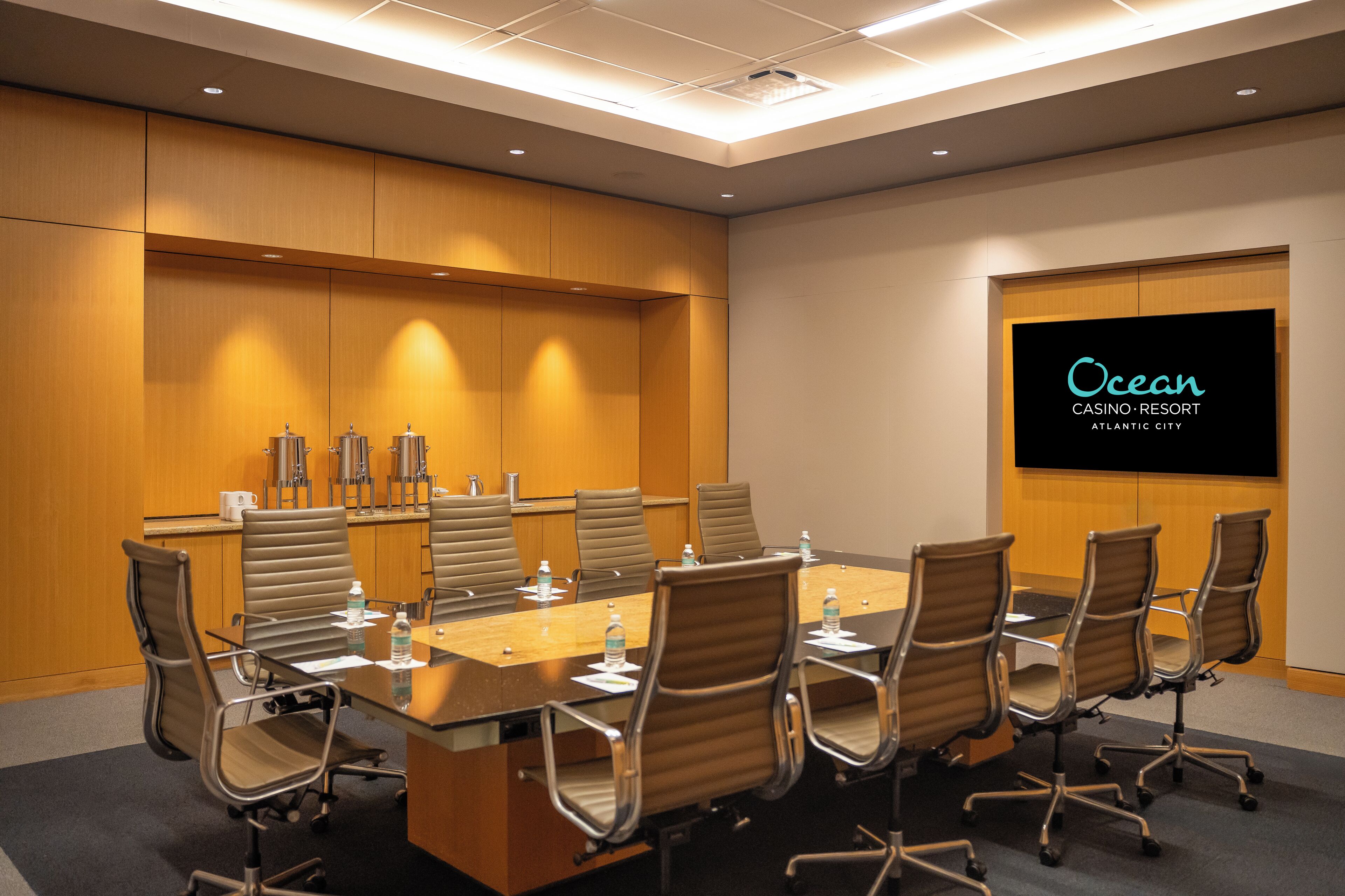 A conference room with a long table, chairs, a projector screen, and a wooden panel wall.
