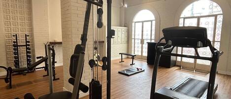 A spacious gym with various exercise equipment, large windows, and a high ceiling.