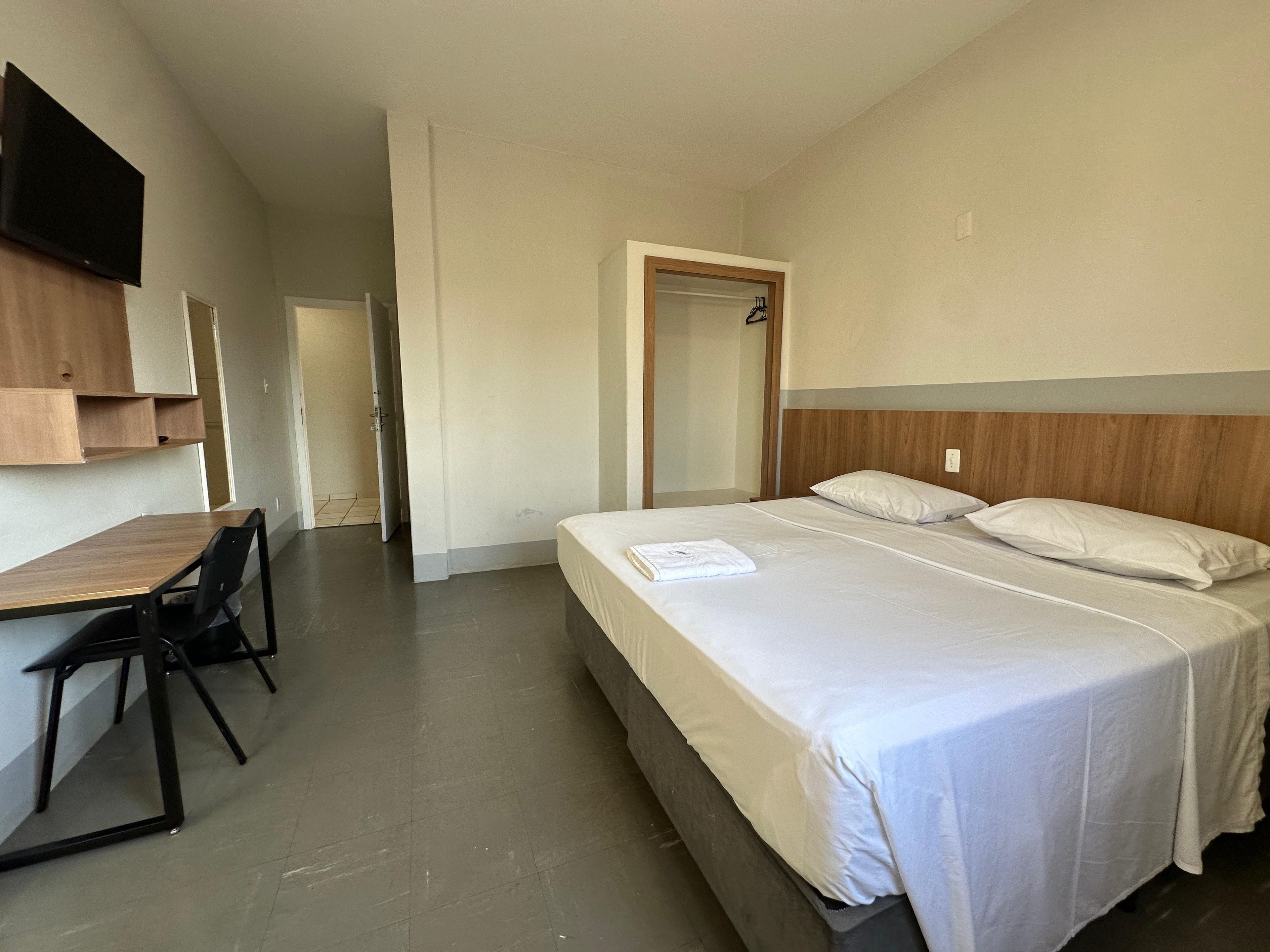 Una camera d'albergo con un letto, una scrivania, una sedia e una televisione.