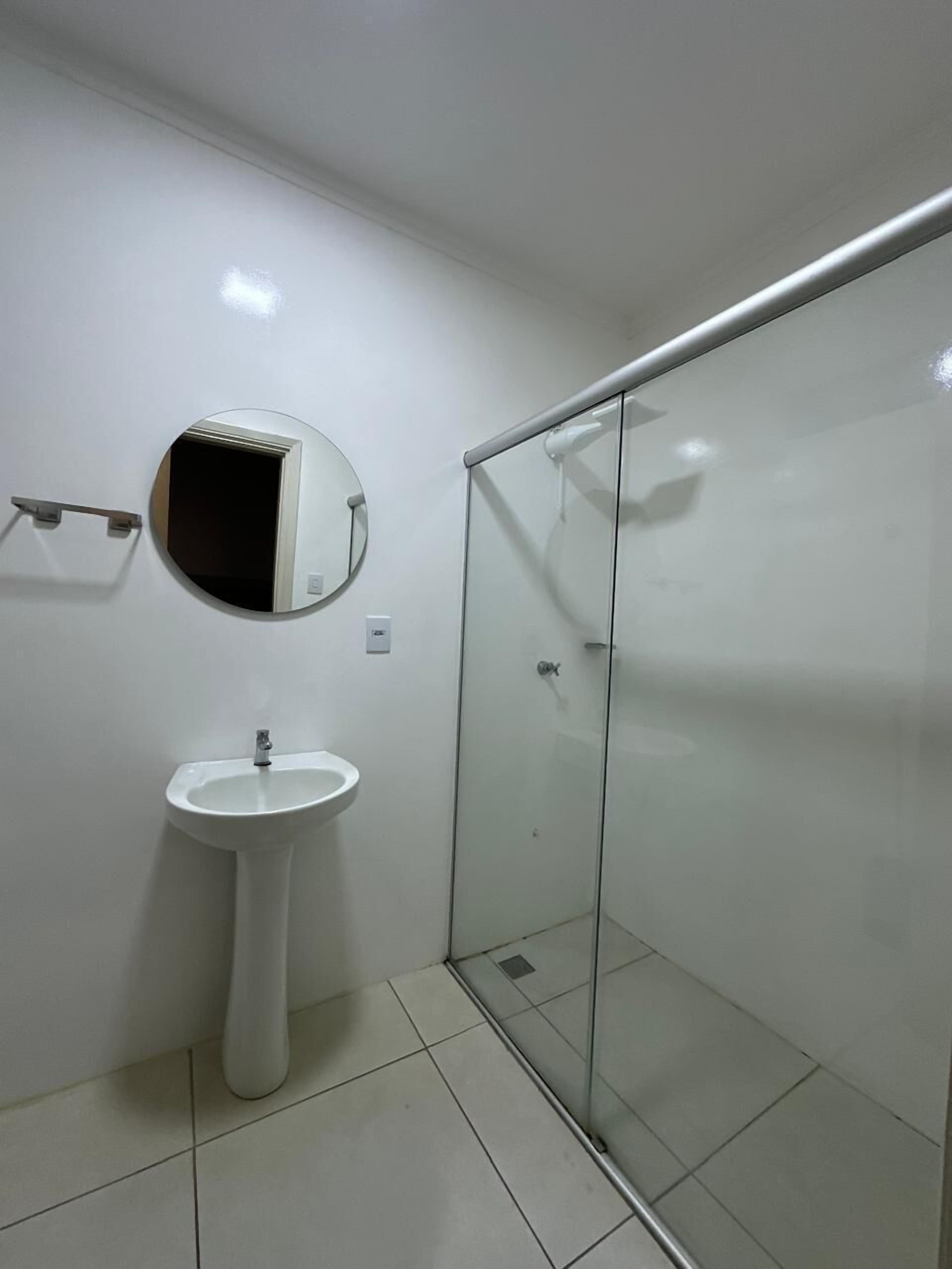 Un baño moderno con cabina de ducha de vidrio, lavamanos pedestal y un espejo redondo.