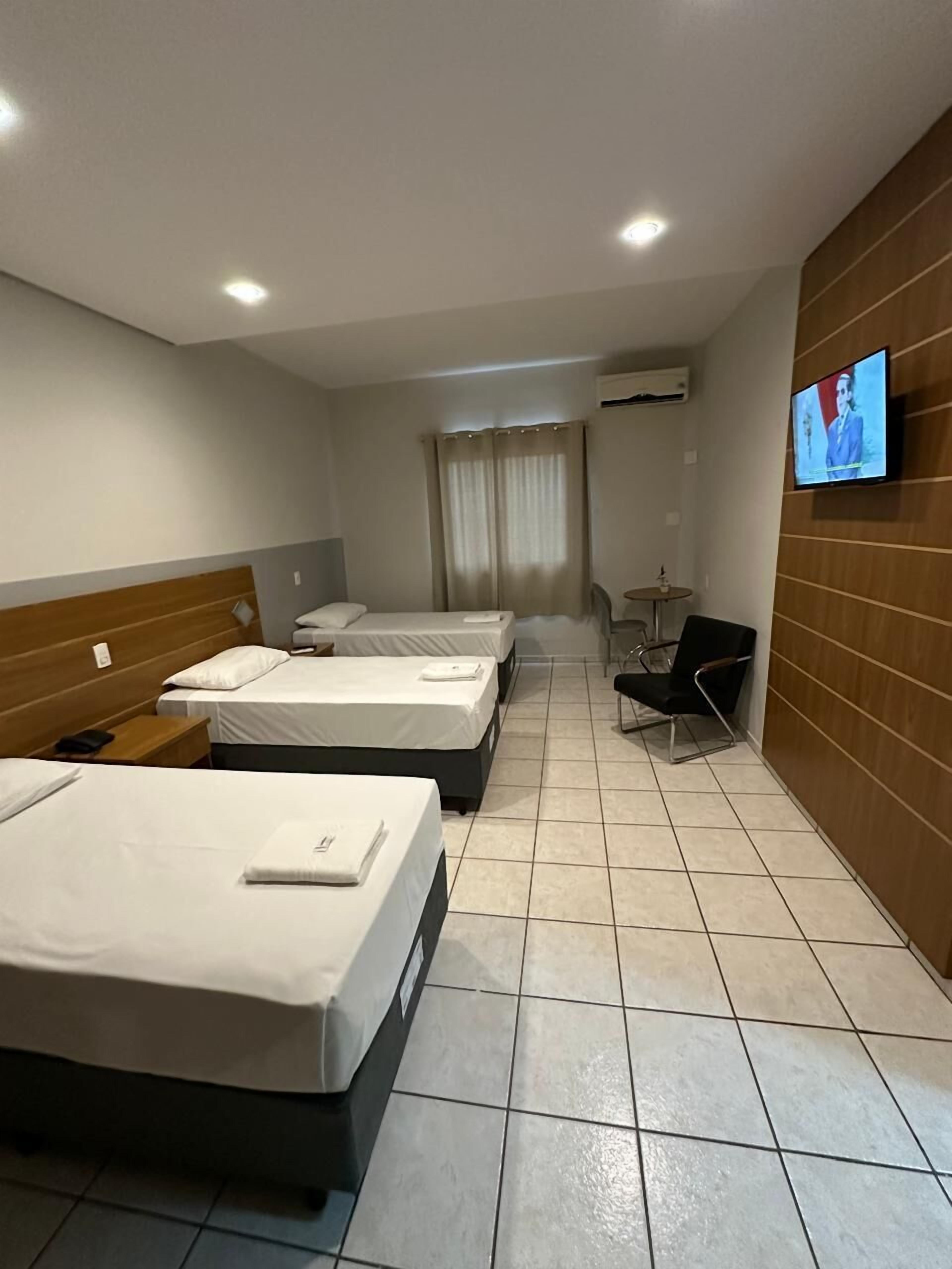 Habitación de hotel con tres camas, un televisor en la pared, una mesita pequeña y una silla.