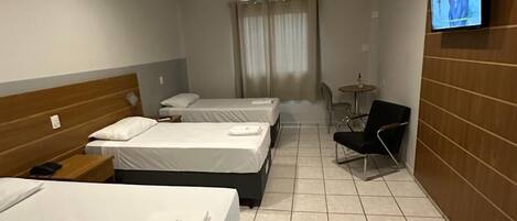 Habitación de hotel con tres camas, un televisor en la pared, una mesita pequeña y una silla.