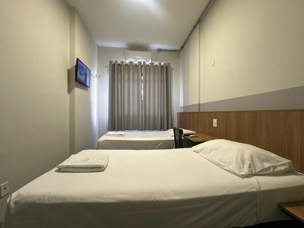 Habitación de hotel con dos camas, un televisor en la pared y una ventana con cortinas.
