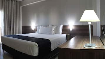 A hotel room with a large bed, a desk with a lamp, and a window with curtains.