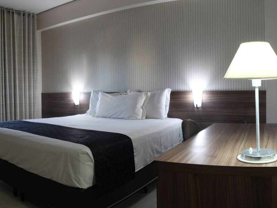 Hotellihuone, jossa on suuri sänky, työpöytä lampun kanssa ja ikkuna, jossa on verhot.