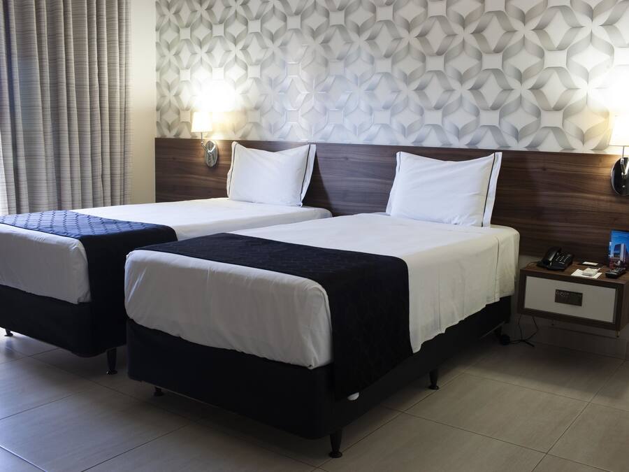 A hotel room with two beds, a nightstand, and a patterned wall.