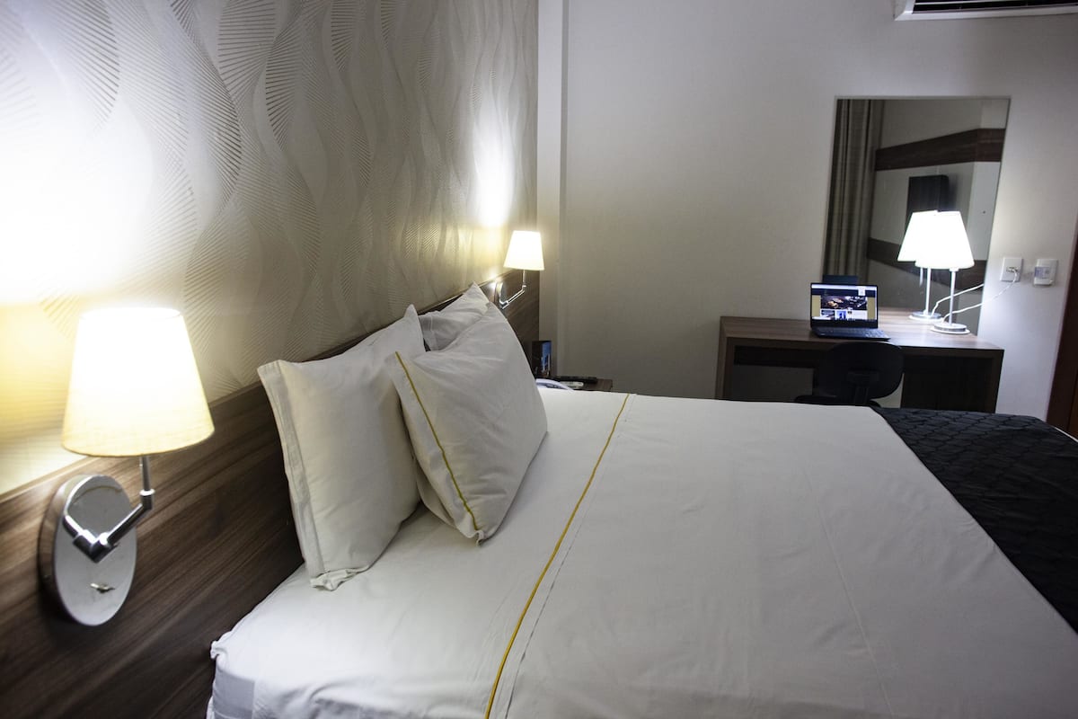 Ett hotellrum med en väl bäddad säng, två sänglampor, ett skrivbord med en bärbar dator och en spegel.