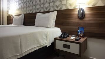Une chambre d’hôtel avec deux lits, une tête de lit en bois, une table de chevet avec un téléphone, des télécommandes et une lampe.