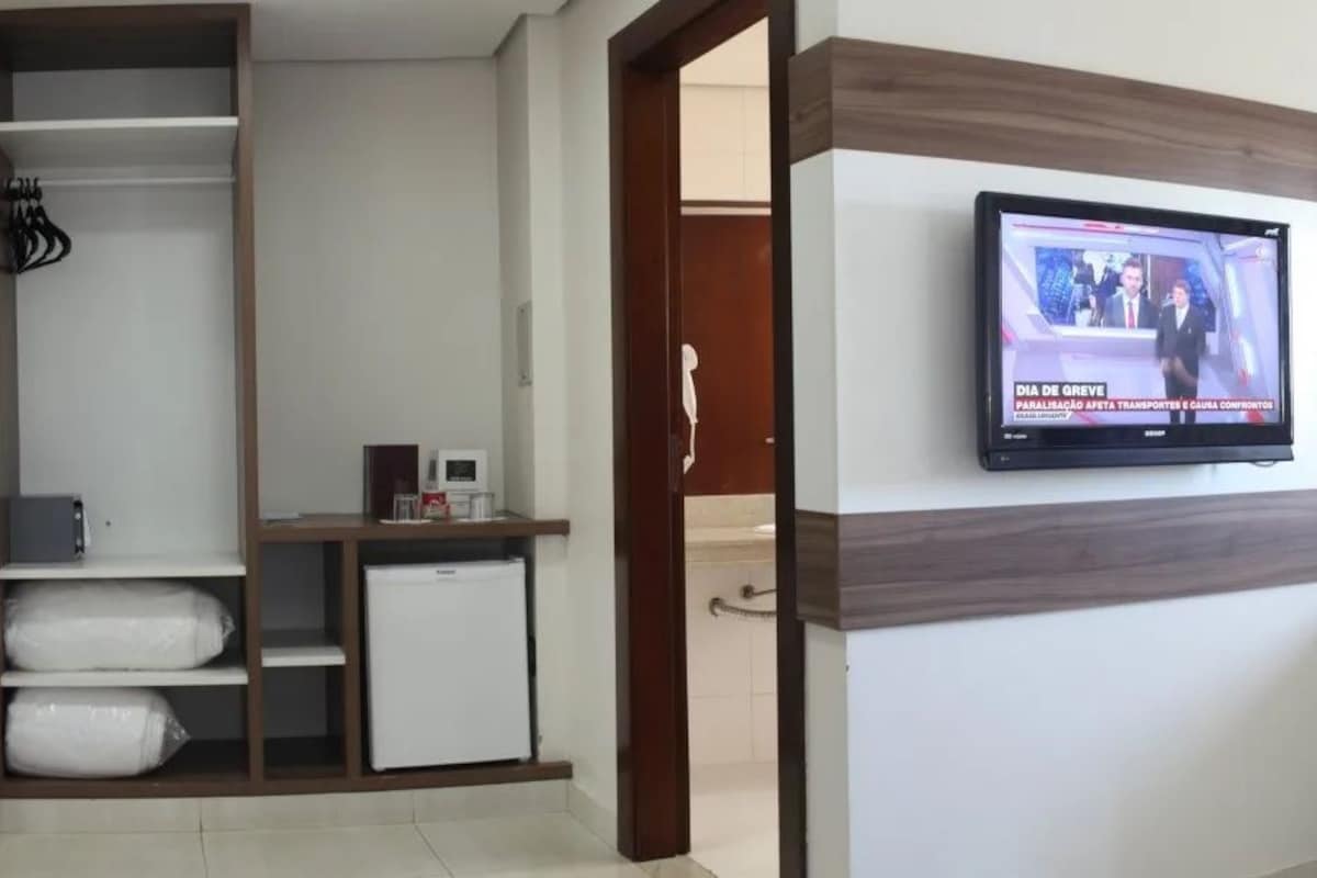 Habitación de hotel con una televisión montada en la pared, una cama con colcha estampada, un escritorio con ordenador y un armario.