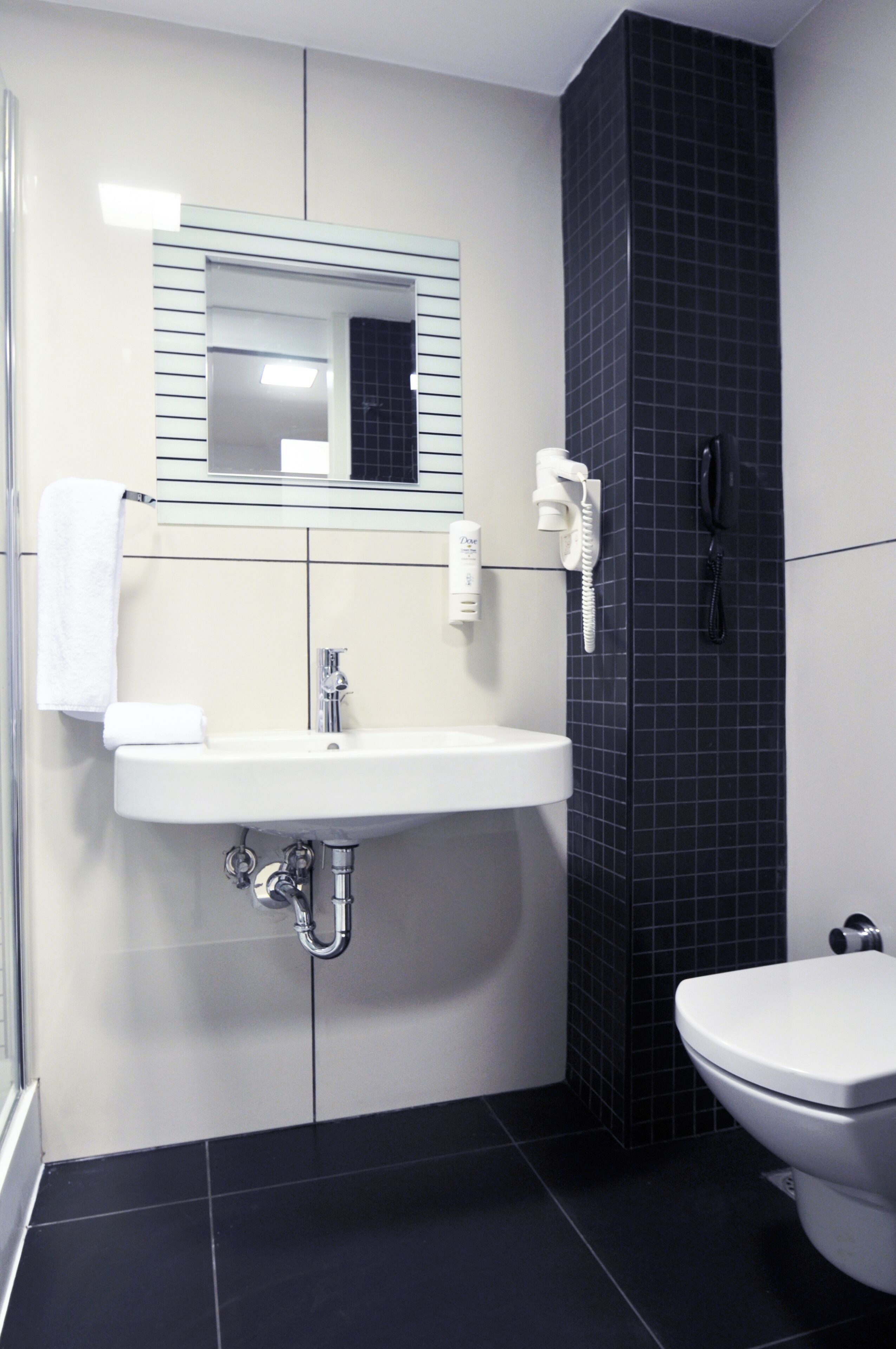 Un baño con lavamanos blanco, un espejo, inodoro y zona de ducha.