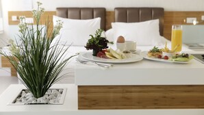 A hotel room with a bed, a breakfast table with plates of food, a glass of orange juice, and a plant on the side.