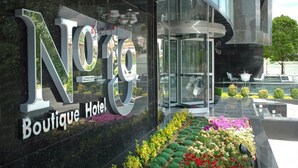 A modern hotel entrance with a glass facade, a rotating door, and a well-maintained flower bed.