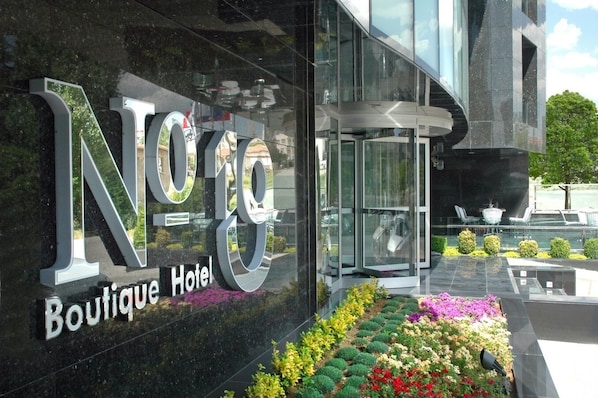 A modern hotel entrance with a glass facade, a rotating door, and a well-maintained flower bed.