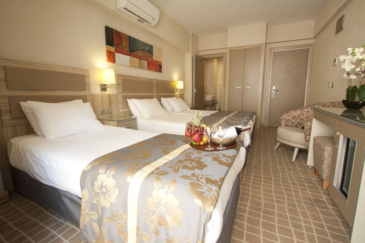 A hotel room with two beds, a desk with a chair, a small bathroom, and a decorative wall piece.
