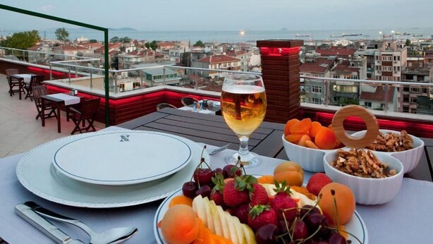 Ein Tisch ist für eine Mahlzeit gedeckt, mit Tellern, Besteck und einem Weinglas auf einer Terrasse mit Blick auf die Stadt.