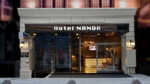 Ein mehrstöckiges Hotel mit klassischer Architektur, mit Balkonen und einem markanten Eingang, der die Beschriftung "Hotel NANDA" trägt.