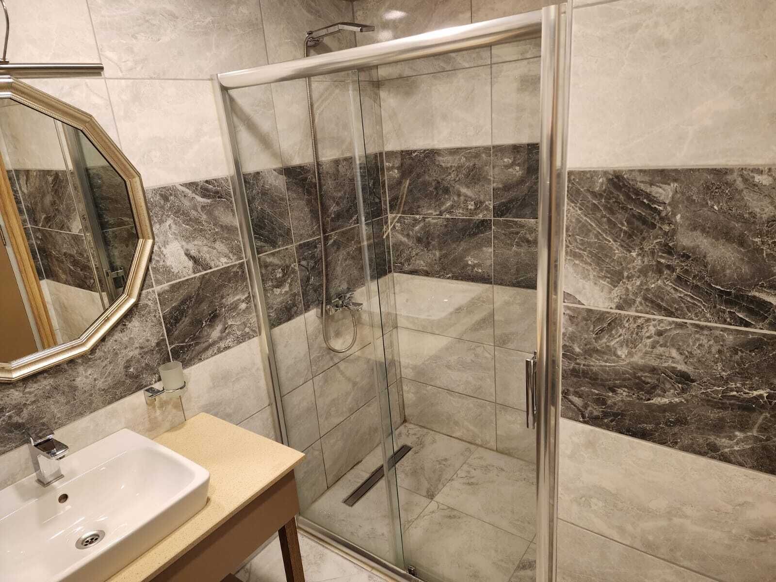A bathroom with a glass shower enclosure, a sink, and a mirror.