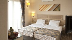 Ein Hotelzimmer mit zwei Betten, einem Fernseher, einer Wand-Klimaanlage und einer Obstschale auf dem Nachttisch.
