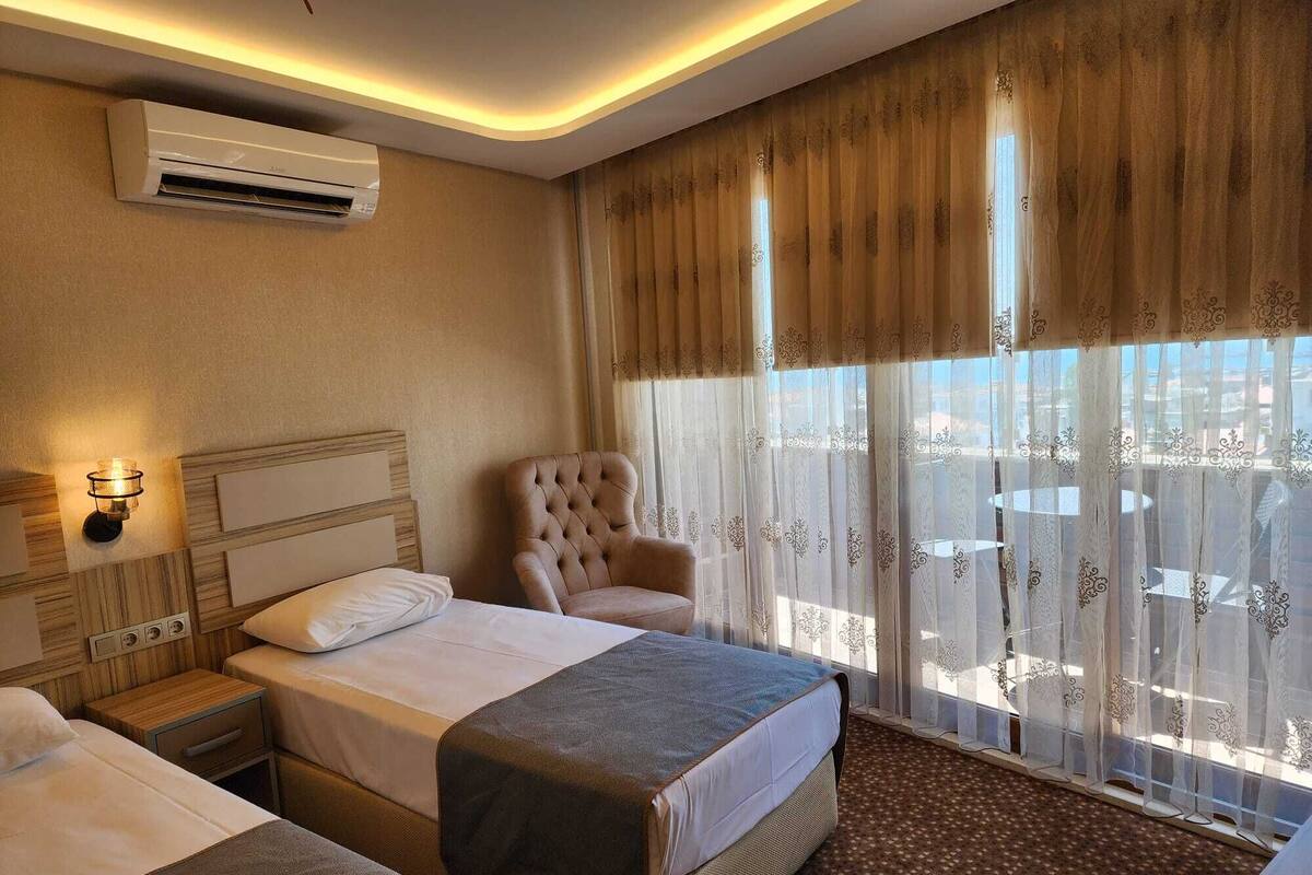 A hotel room with a bed, a chair, an air conditioner, and a window with curtains.