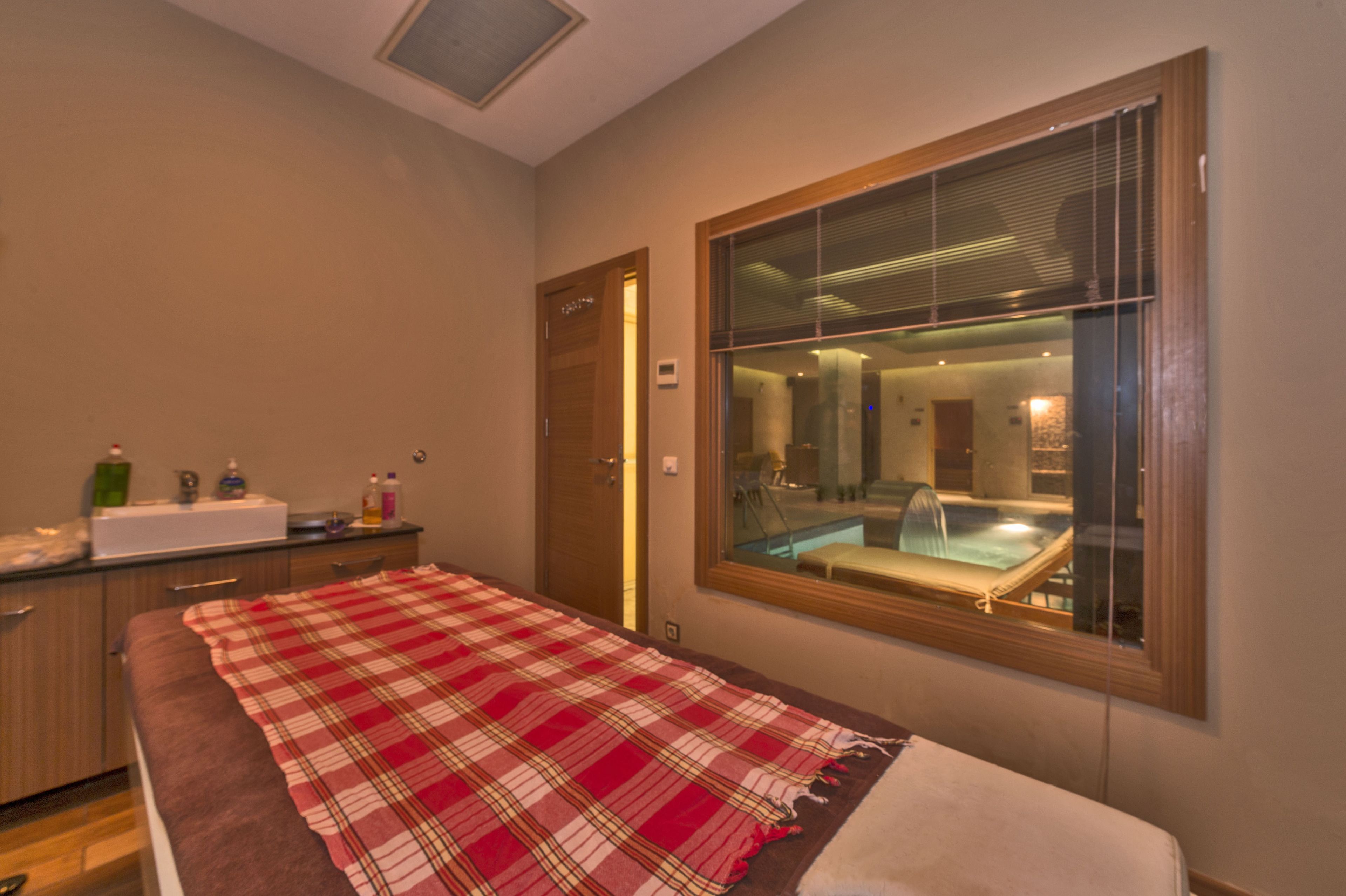 Un dormitorio con un ventanal grande, una cama con manta escocesa, una mesita de noche con artículos de aseo personal y vistas a un área de spa.